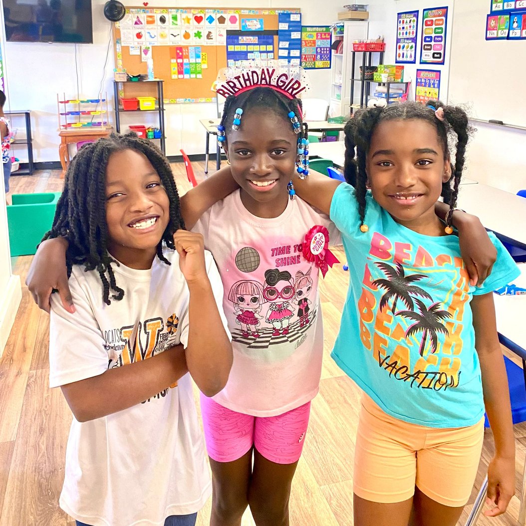 Three children smiling and celebrating in a colorful classroom at Red Trolleys Daycare in Valdosta, GA.