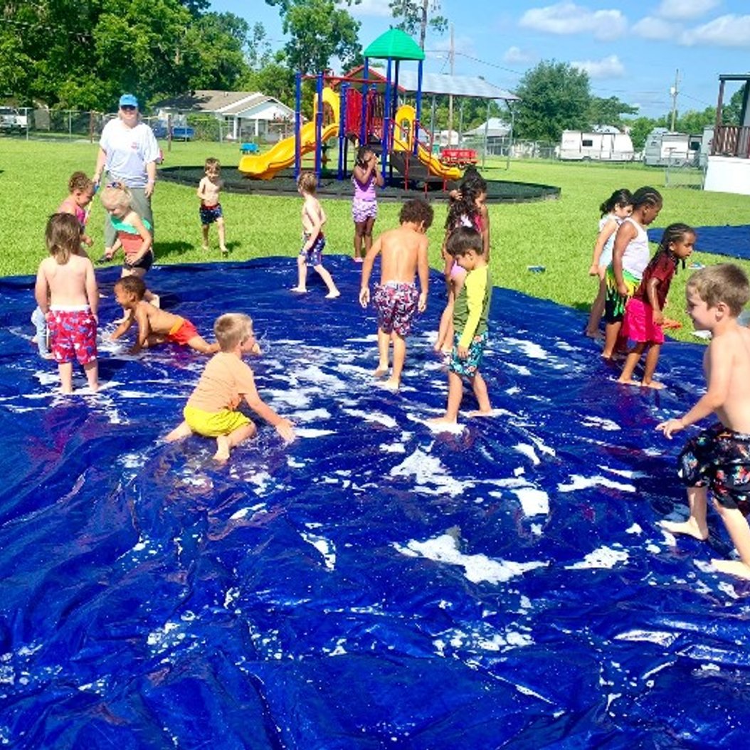 Children enjoying water play activity at summer camp in Valdosta, GA with outdoor playground and clear blue skies.