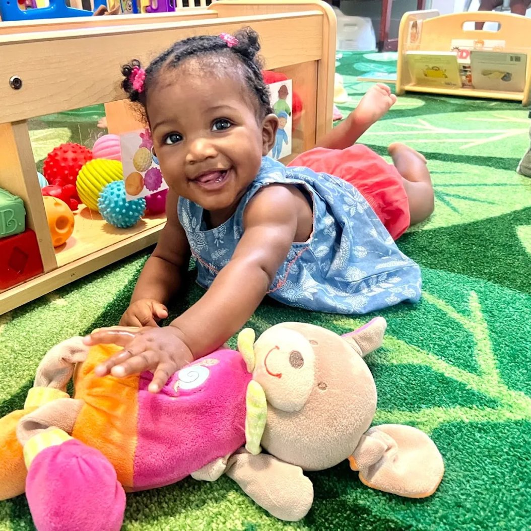 Smiling infant playing with toys at a nurturing care center in Valdosta, GA, for ages 6 weeks to 12 months.