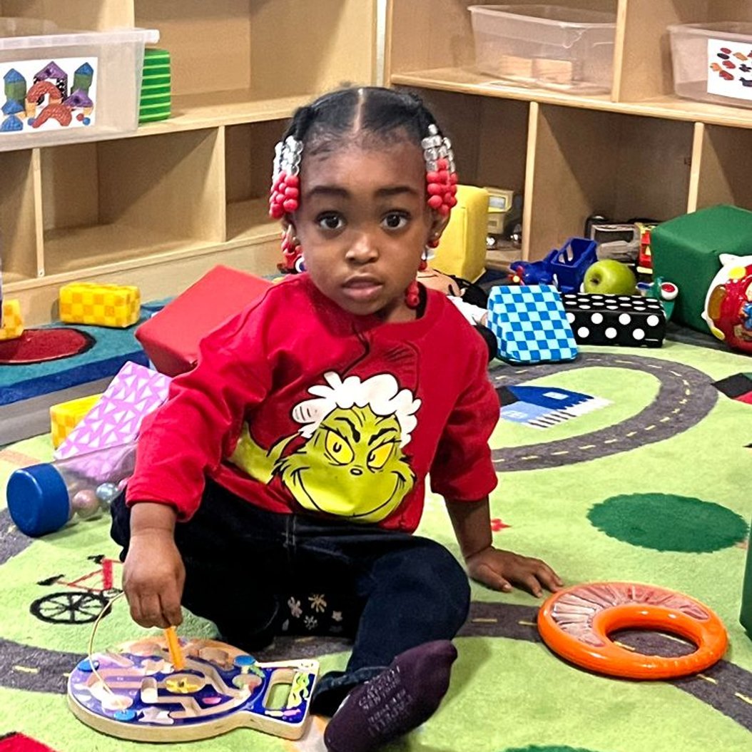Toddler exploring a wooden maze toy on the classroom rug at Active Xplorers daycare in Valdosta, GA.
