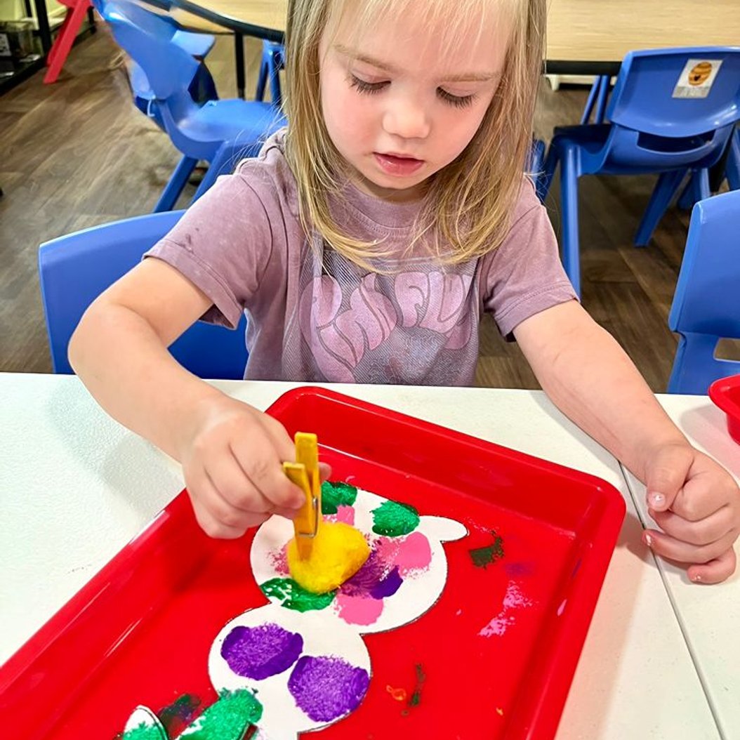 Preschooler creating sponge-painted artwork in a creative hands-on activity at Red Trolleys Daycare in Valdosta, GA.