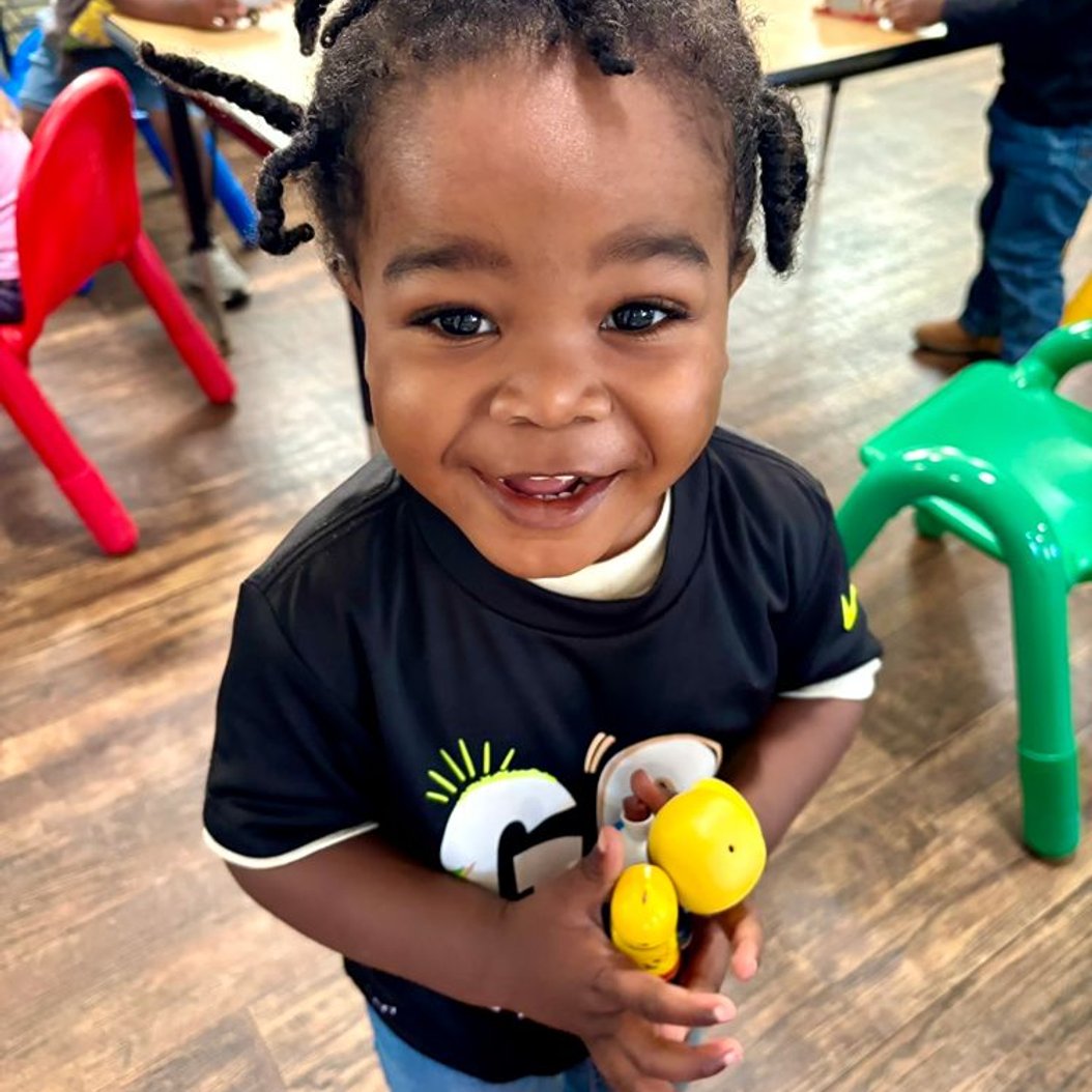 Smiling young toddler holding a toy in the Busy Bees classroom at Red Trolleys Daycare in Valdosta, GA.