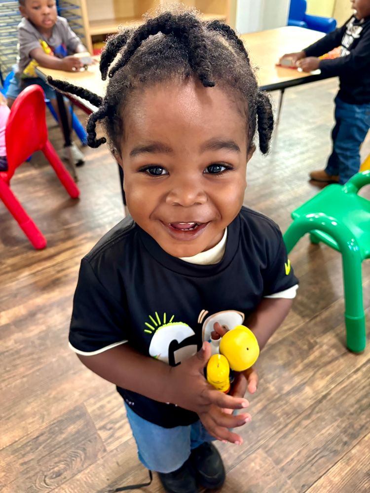 Smiling toddler holding a toy in the classroom at Red Trolleys Daycare in Valdosta, GA.